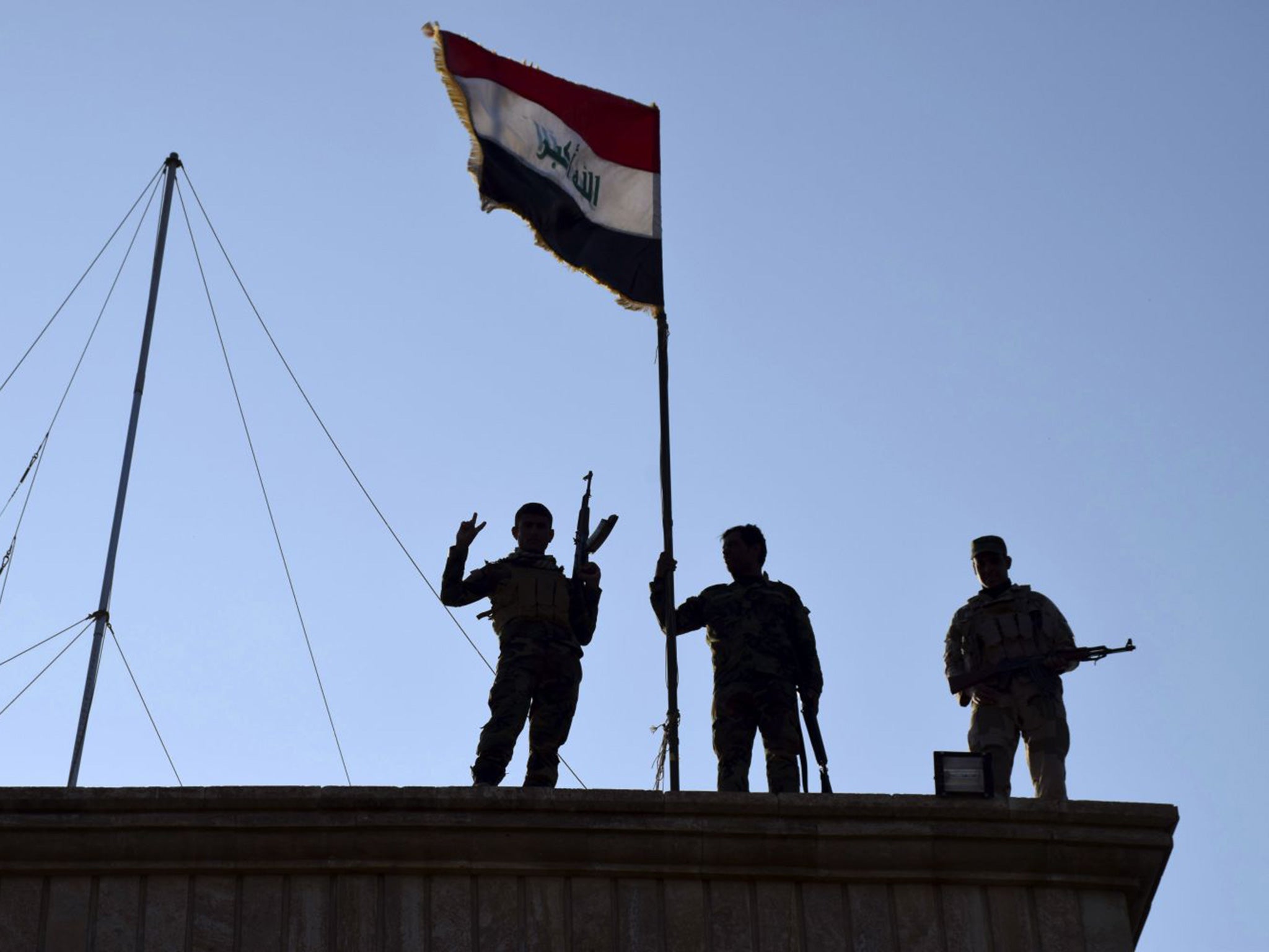 Iraqi soldiers plant the national flag over a government building in Ramadi as security forces advance towards Isis positions