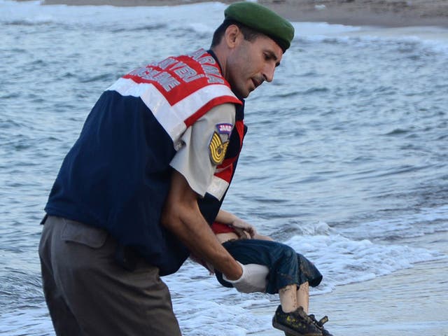 A Turkish police officer carries the body of Aylan Kurdi off the shores in Bodrum