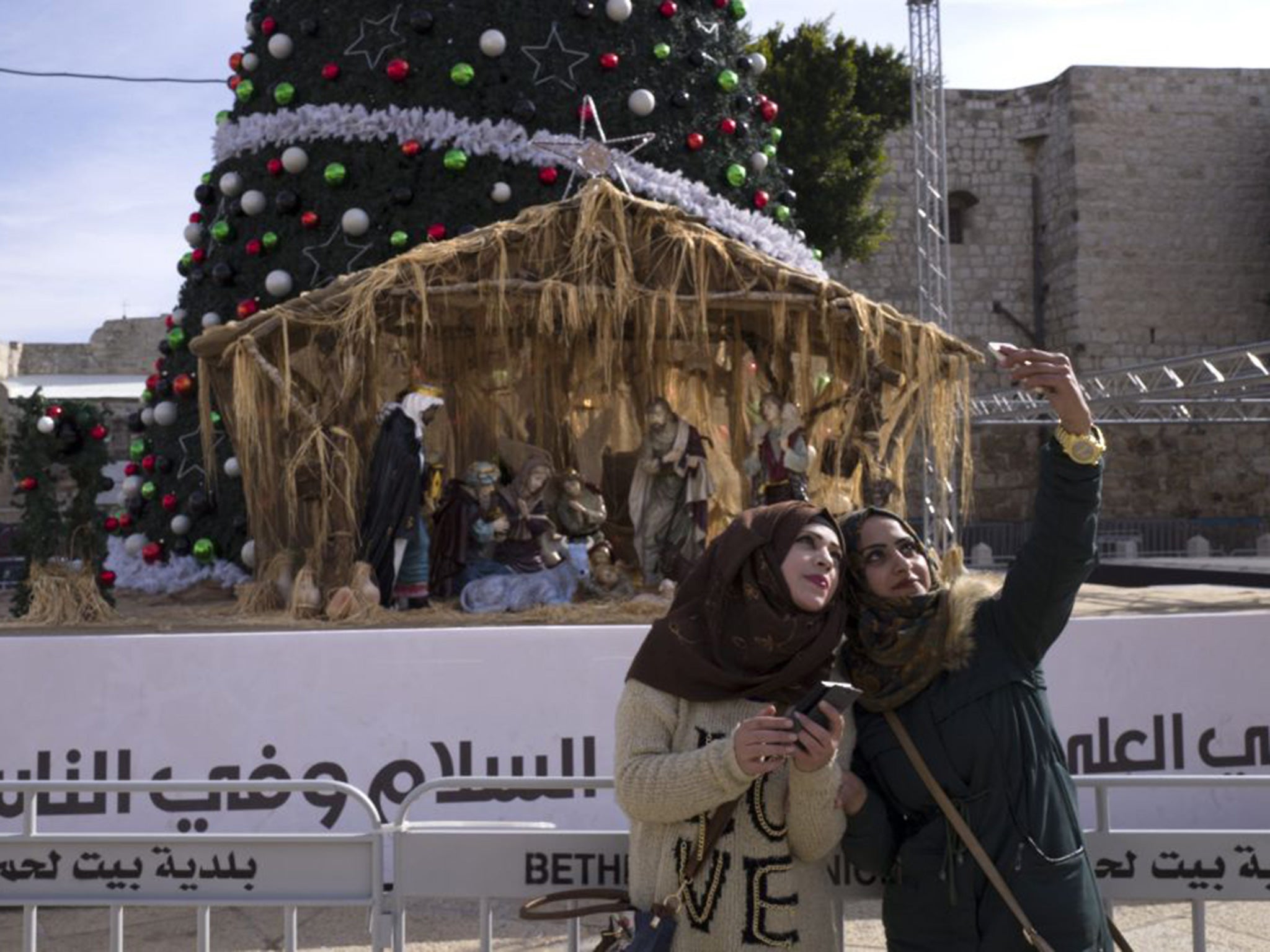 Palestinian women take selfies in front of the Christmas tree and a large Nativity scene in Manger Square in the West Bank town of Bethlehem