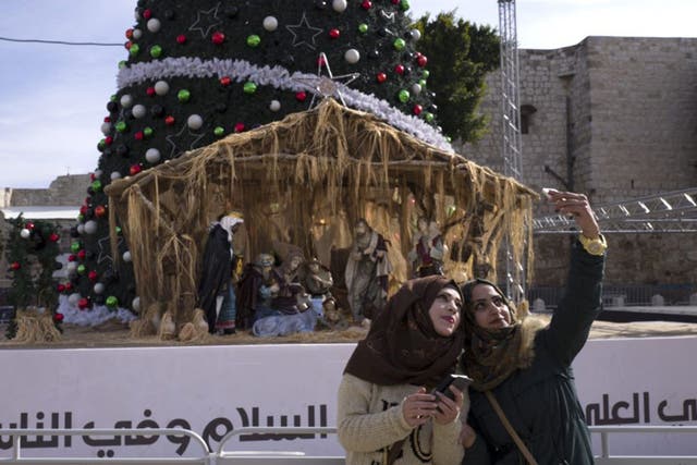 Palestinian women take selfies in front of the Christmas tree and a large Nativity scene in Manger Square in the West Bank town of Bethlehem