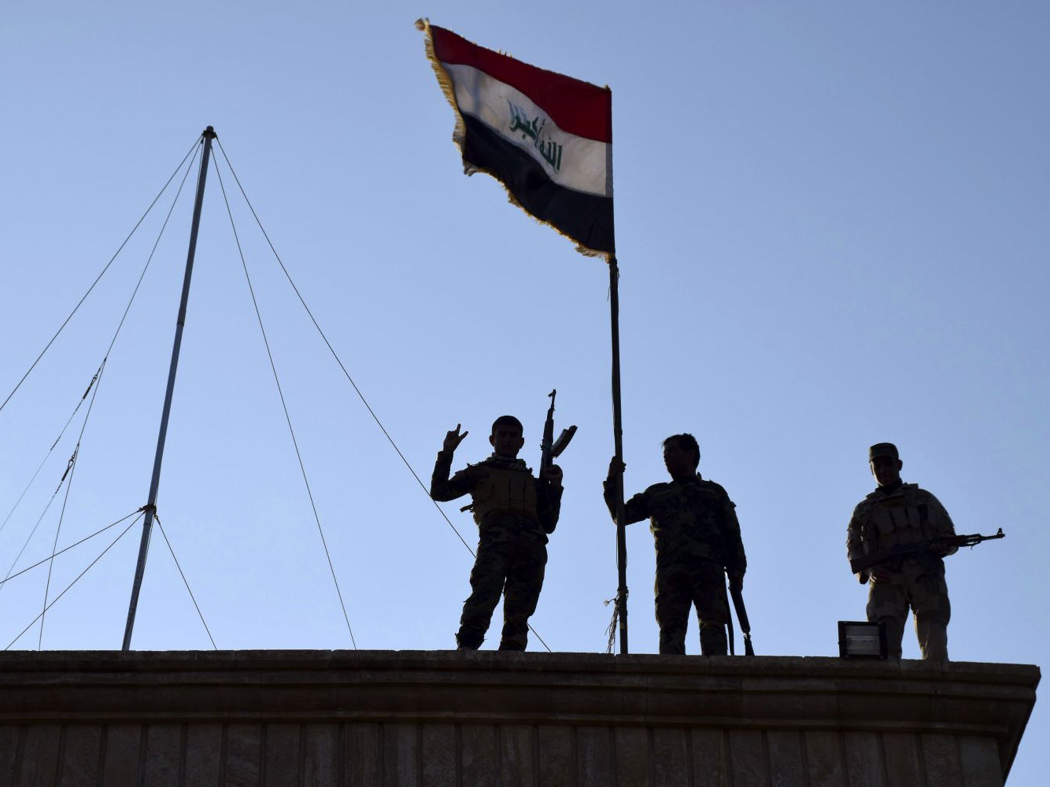 Iraqi soldiers plant the national flag above a government building in Ramadi, 70 miles from Baghdad, on Monday