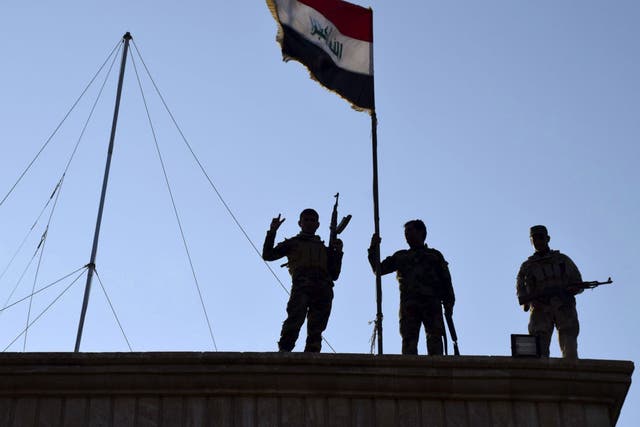 Iraqi soldiers plant the national flag above a government building in Ramadi, 70 miles from Baghdad, on Monday