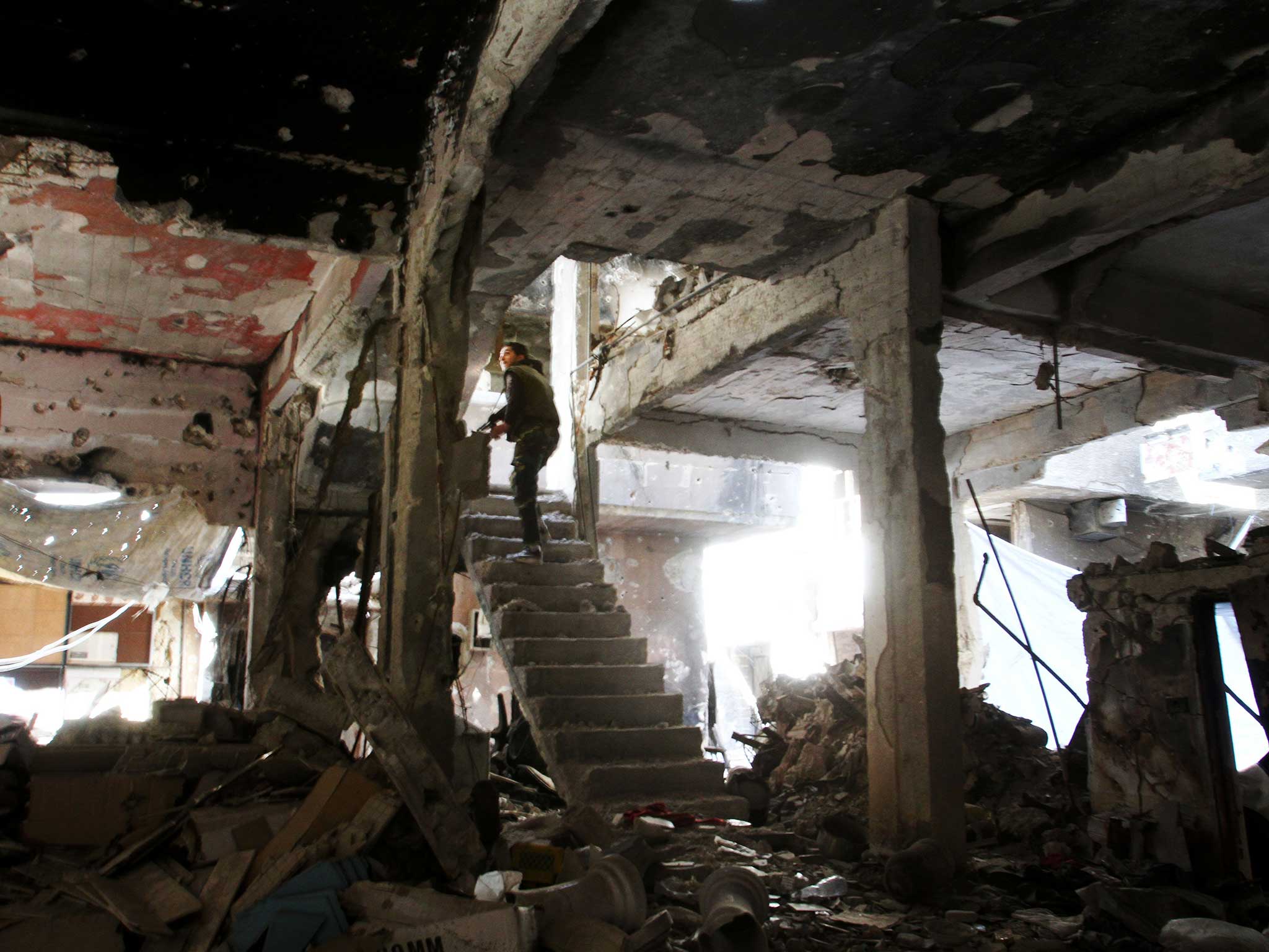 A sniper peers through the ruins of a building in Yarmouk refugee camp
