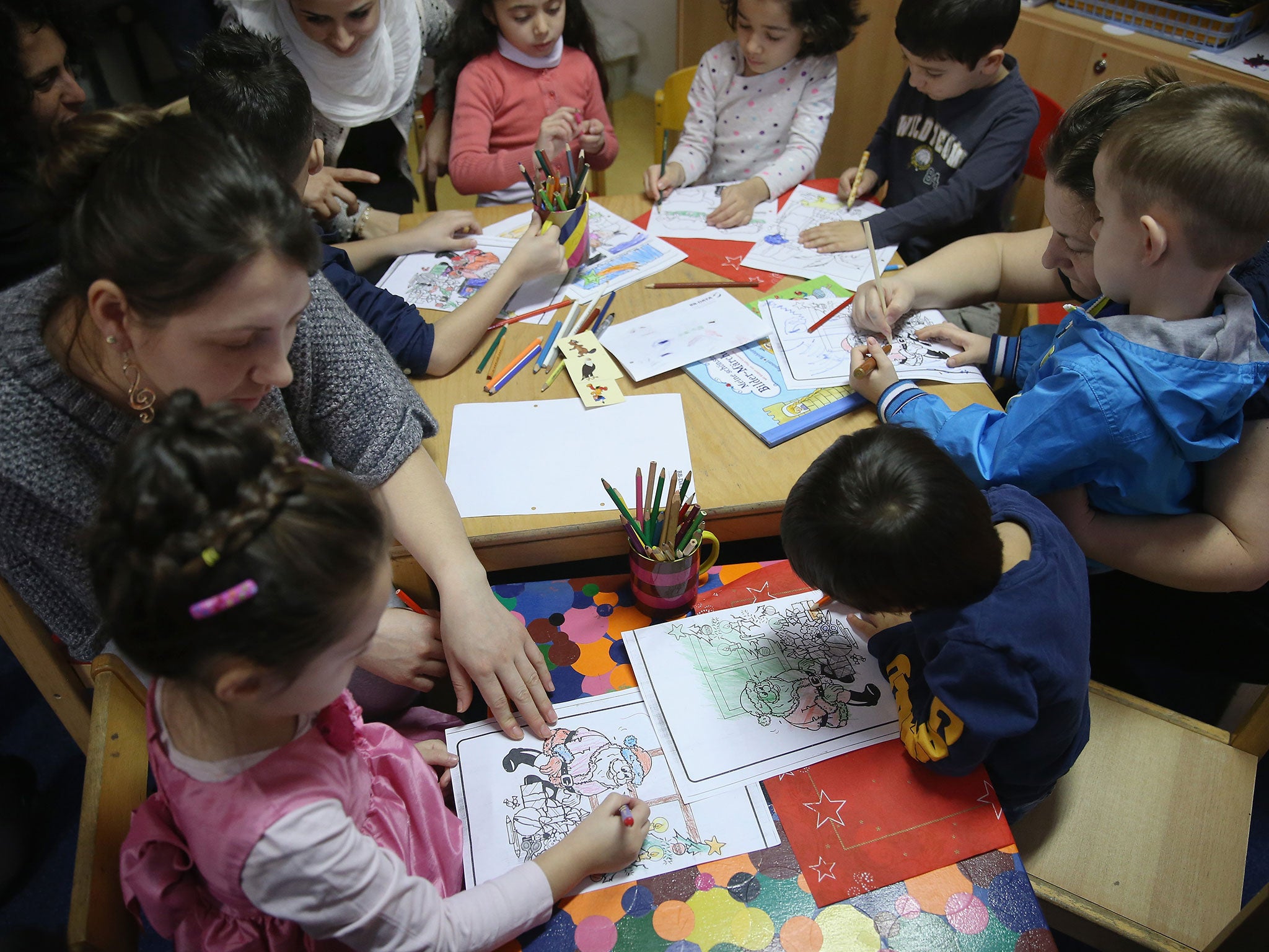 Refugee mothers with their children look through games and books during the presentation of a new initiative to help children of refugees learn to read German at a shelter for migrants and refugees on 16 December, 2015 in Berlin, Germany