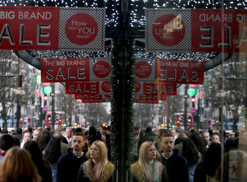 Shoppers are reflected in a store window as they pass sales advertisements on Oxford Street in London