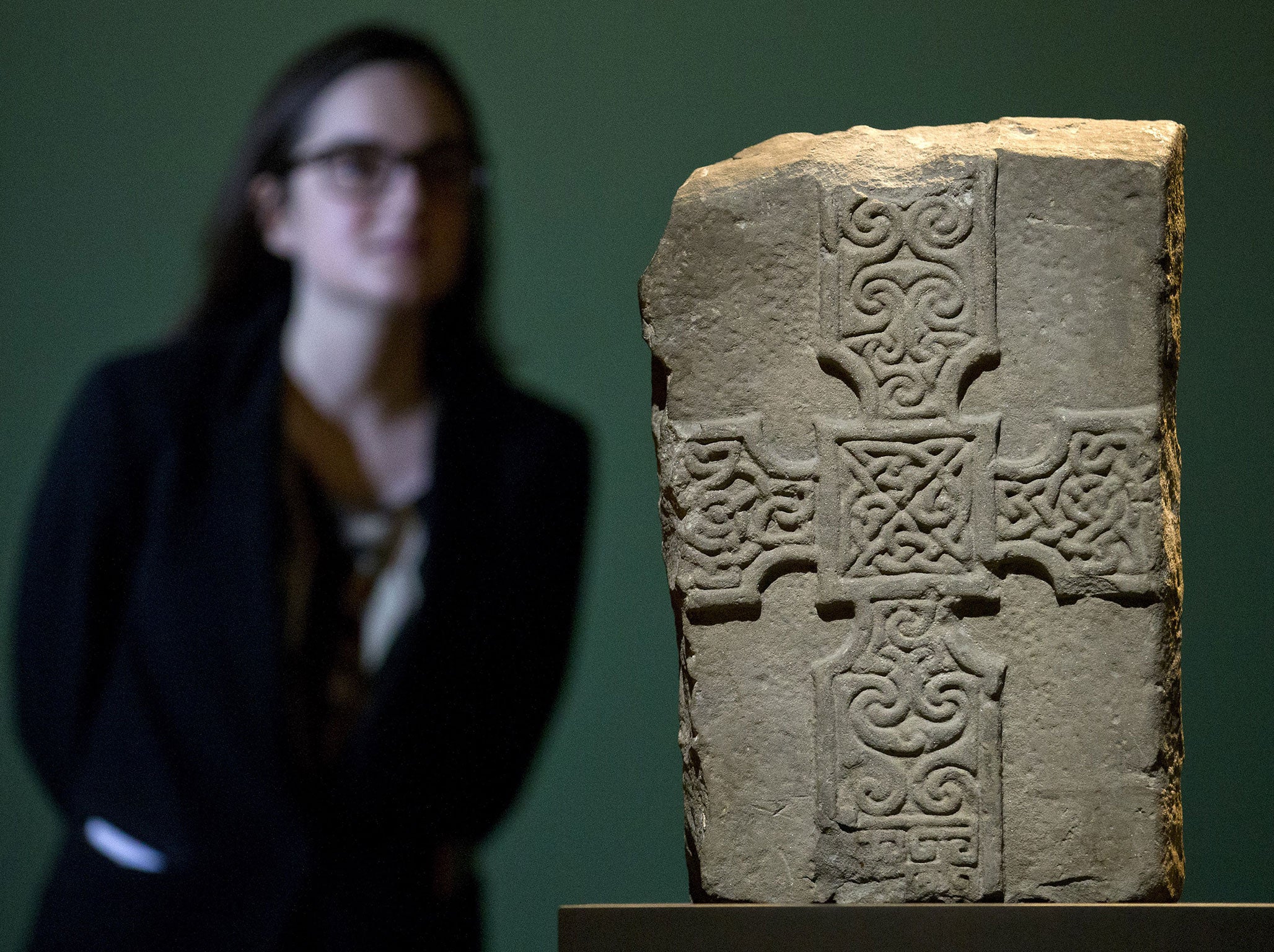 An assistant poses for photographers looking at a sandstone cross-slab, dated to between 800 and 900 AD, during a press preview of 'Celts: art and identity' exhibition at the British Museum in London on September 23, 2015