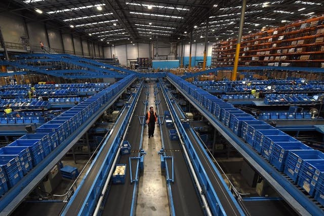 A worker walks alongside a conveyor belt as items are sorted into crates to be sent to retail stores from the Argos Distribution Centre in Burton-upon-Trent, central England