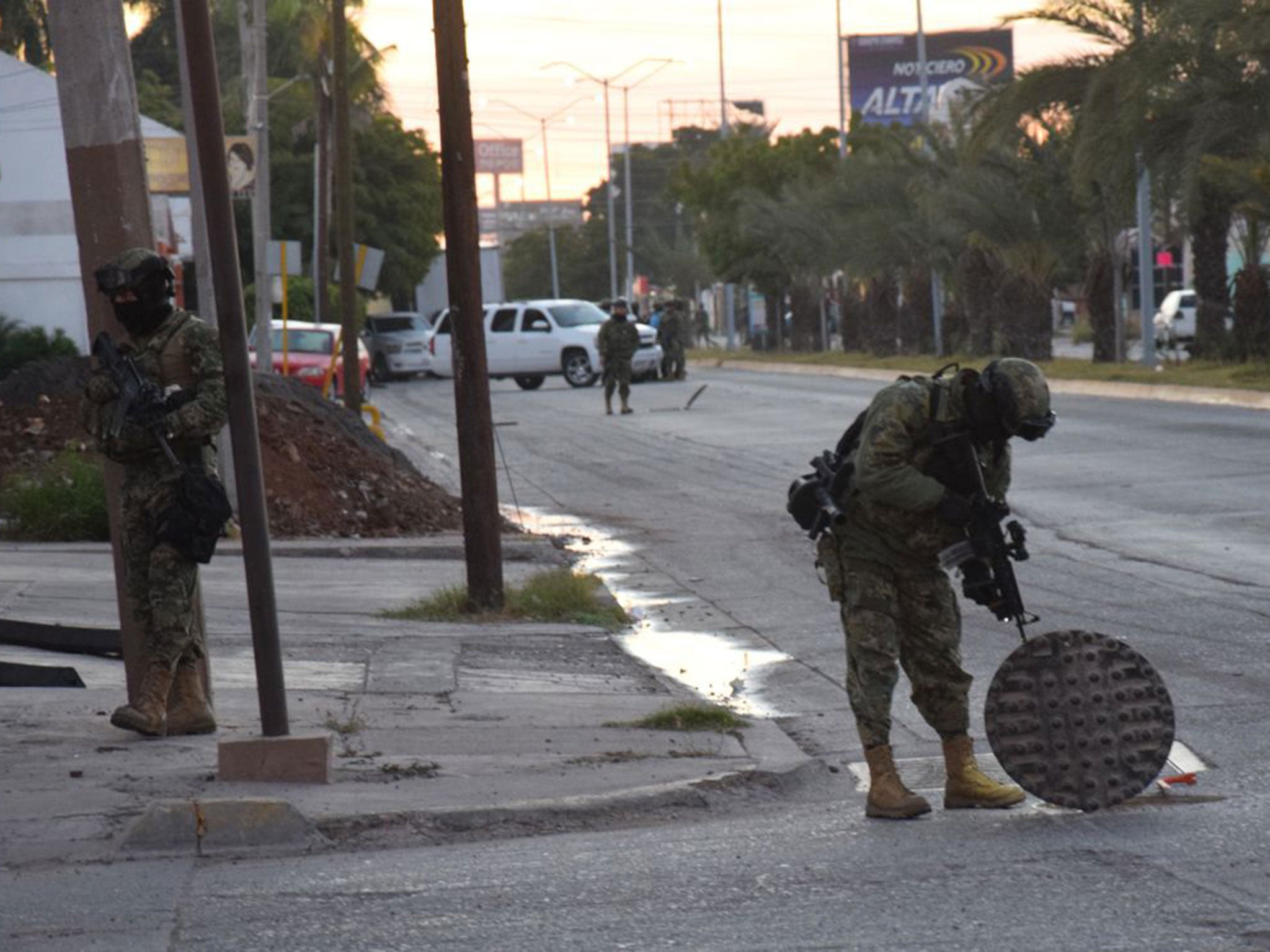 A soldier looks down a manhole as part of a security operation following El Chapo's attempts to evade police via the city's drainage system