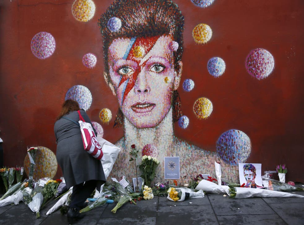 A woman leaves a bouquet at a mural of David Bowie in Brixton