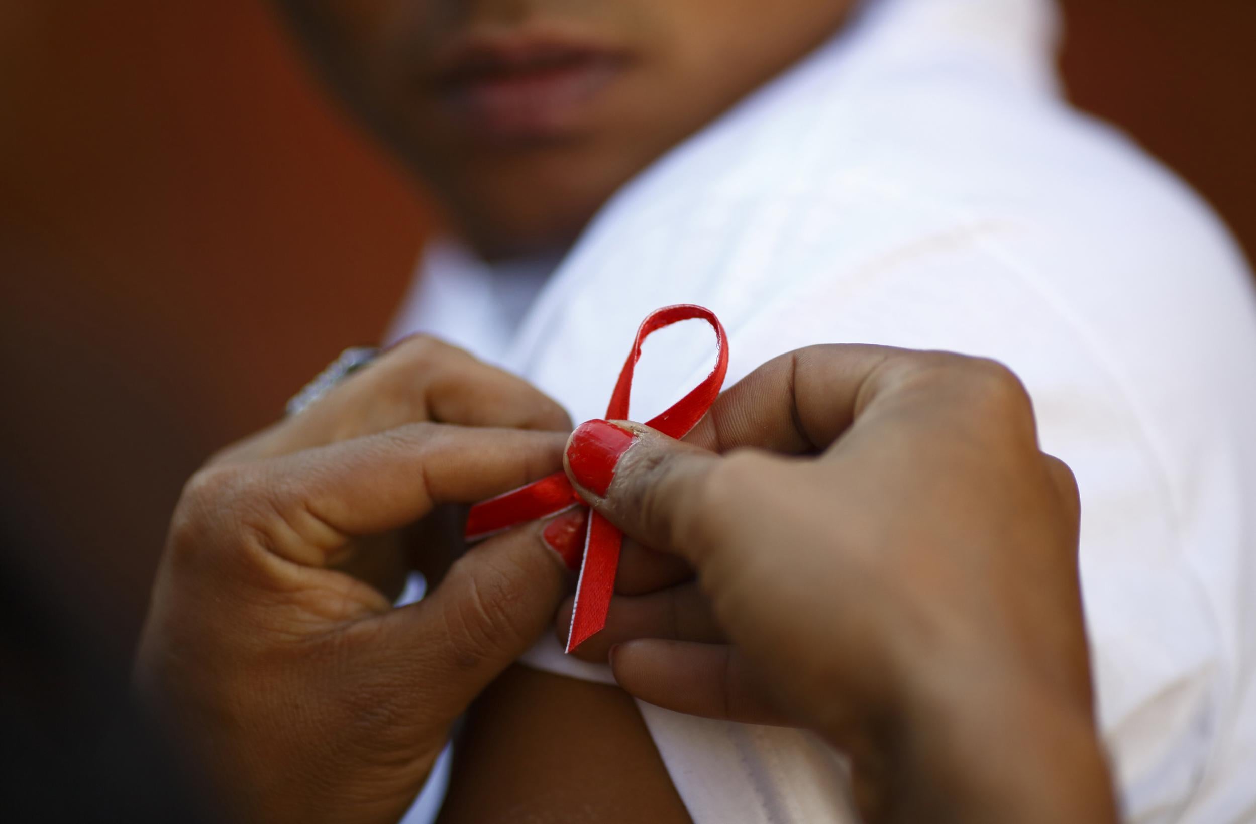 A red ribbon is put on the sleeves of a man by his friend to show support for people living with HIV