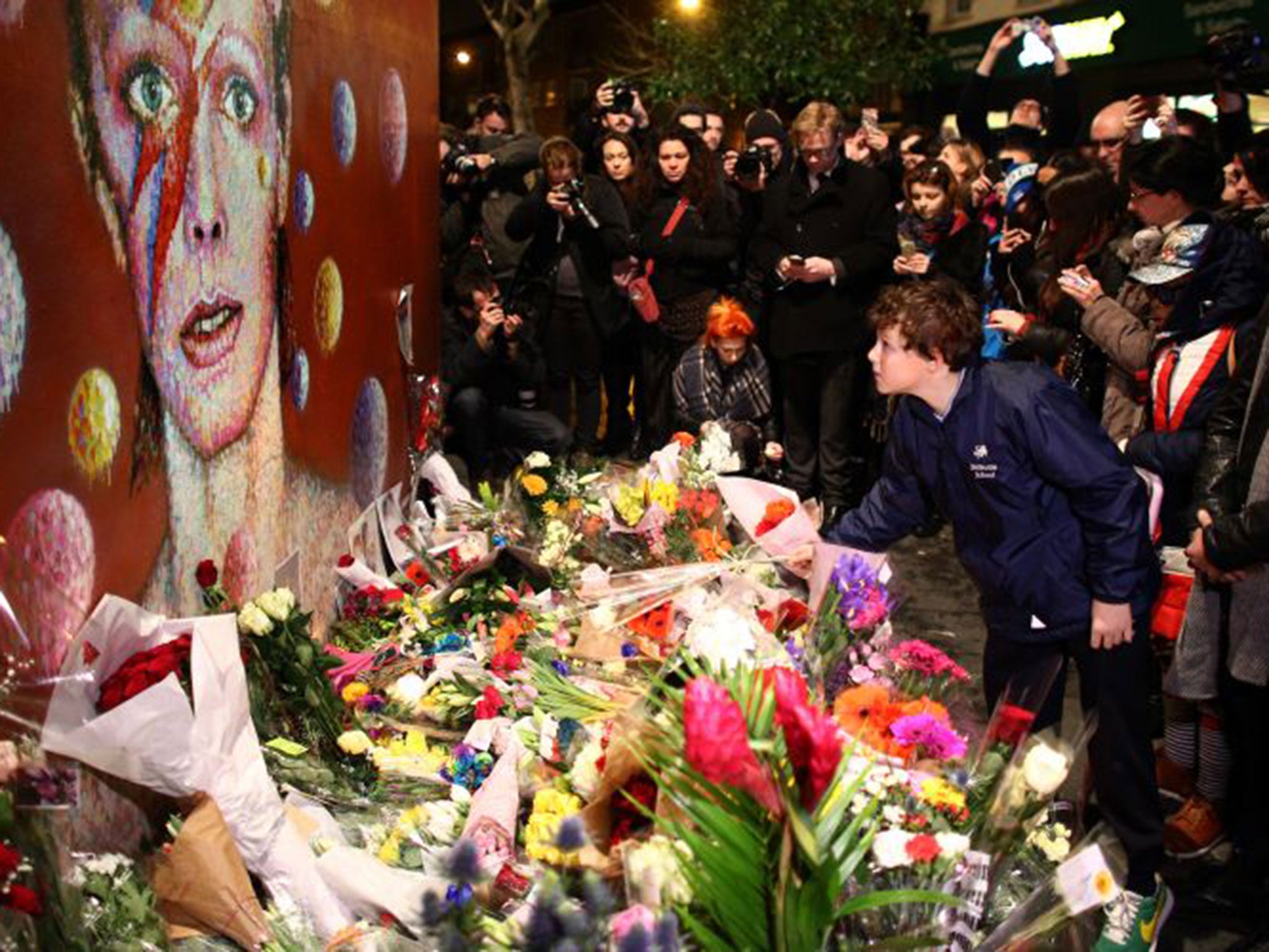 A boy leaves flowers beneath the mural of David Bowie in Brixton, London