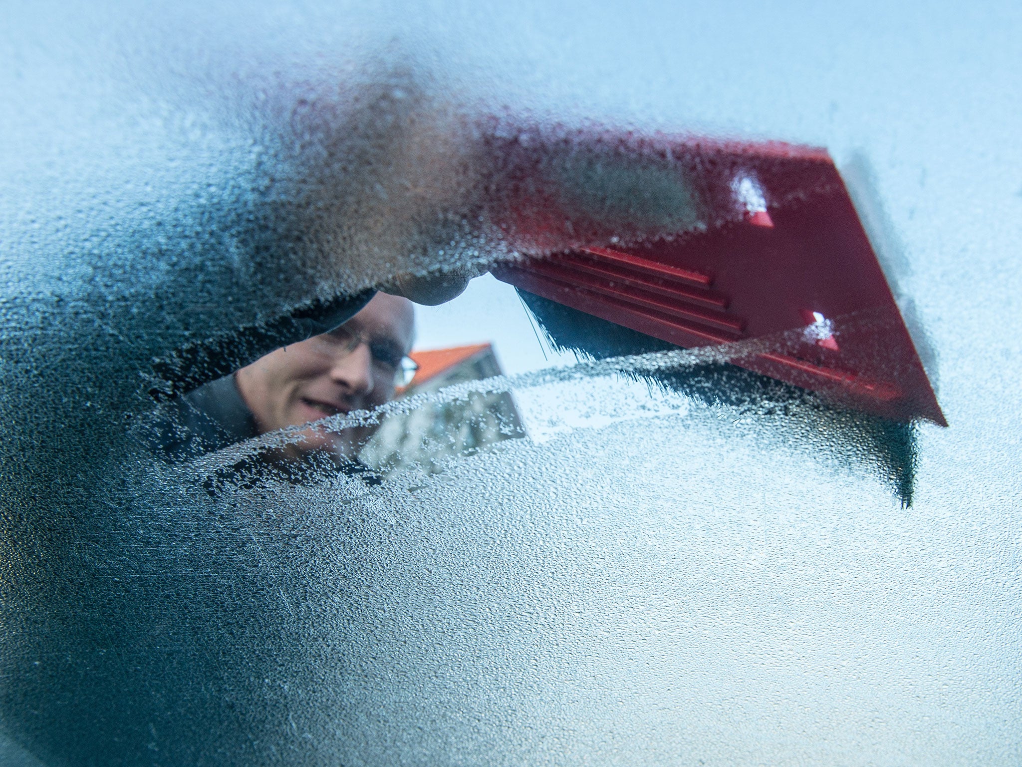 A man removes frost from his windscreen using an ice scraper