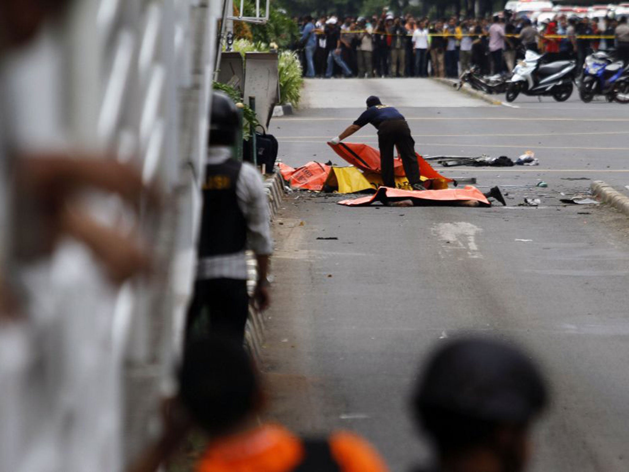 An Indonesian police officer placing body bags on victims at the scene of a bomb blast in Jakarta yesterday; a police officer and a Canadian died in the attacks