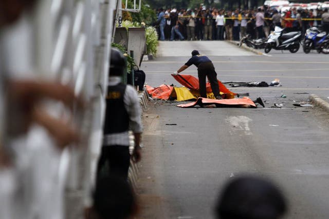 An Indonesian police officer placing body bags on victims at the scene of a bomb blast in Jakarta yesterday; a police officer and a Canadian died in the attacks