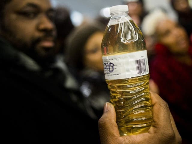 A pastor holds up a bottle of Flint water during protests outside Michigan Governor Rick Snyder's office on Thursday 14 January