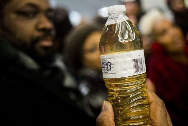 A pastor holds up a bottle of Flint water during protests outside Michigan Governor Rick Snyder's office on Thursday 14 January