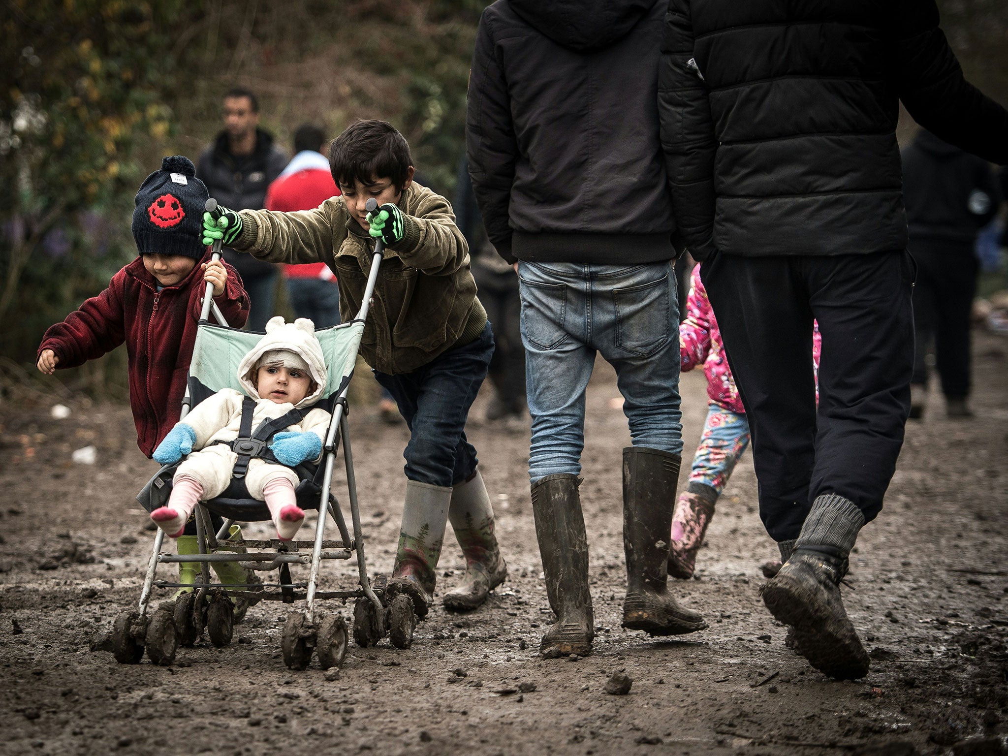 Young refugees walk with a stroller in a camp in Grande-Synthe