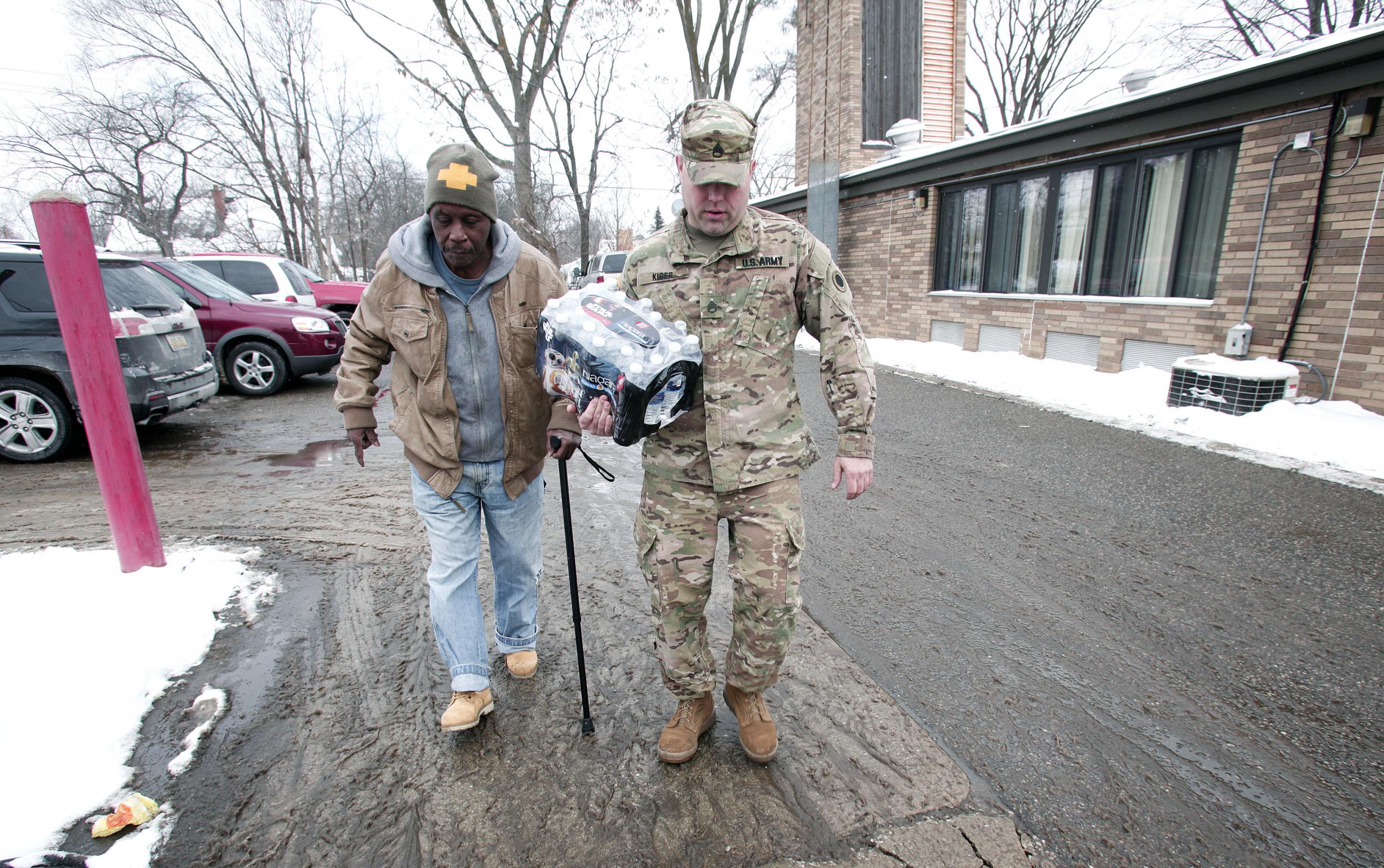 Michigan National Guard Staff Sergeant Steve Kiger of Beaverton, Michigan, helps a Flint, Michigan resident take bottled water out to his car
