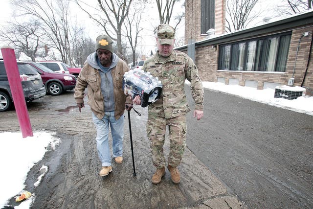 Michigan National Guard Staff Sergeant Steve Kiger of Beaverton, Michigan, helps a Flint, Michigan resident take bottled water out to his car