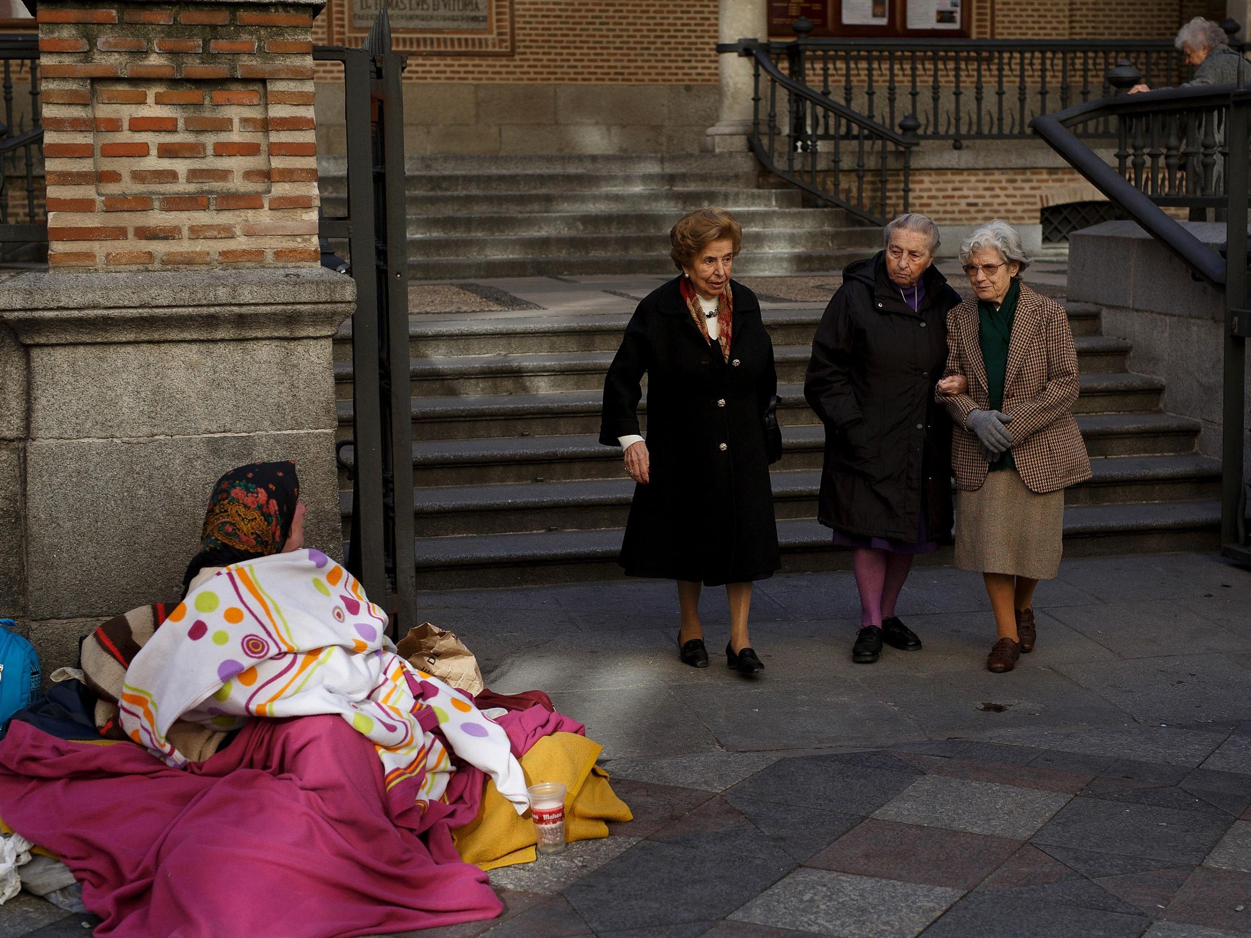 A woman begs in the street as women walk past on November 26, 2015 in Madrid, Spain. According to a recent study Madrid was ranked the most segregated city in Europe between rich and poor.