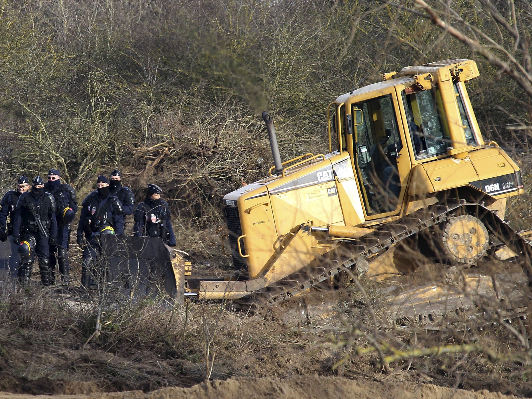 Police officers walk past a bulldozer in the Calais refugee camp, northern France Monday, Jan.18, 2016