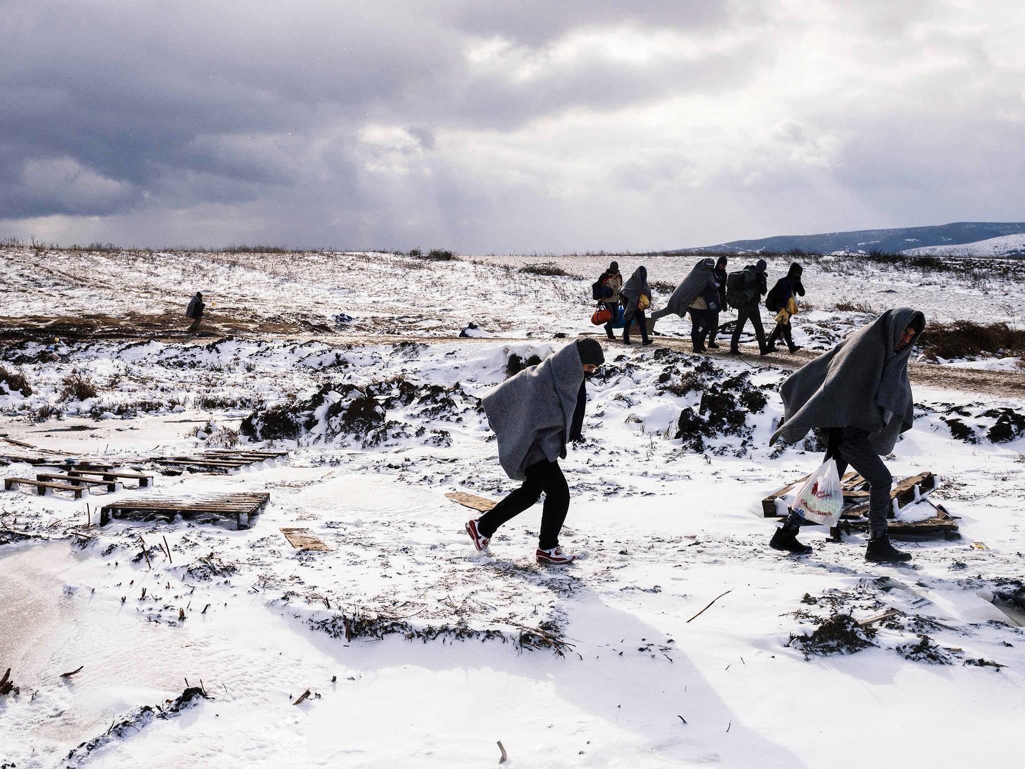 Refugees use their sleeping blankets to keep warm as they walk along snow covered fields after crossing the Macedonian border into Serbia, near the village of Miratovac