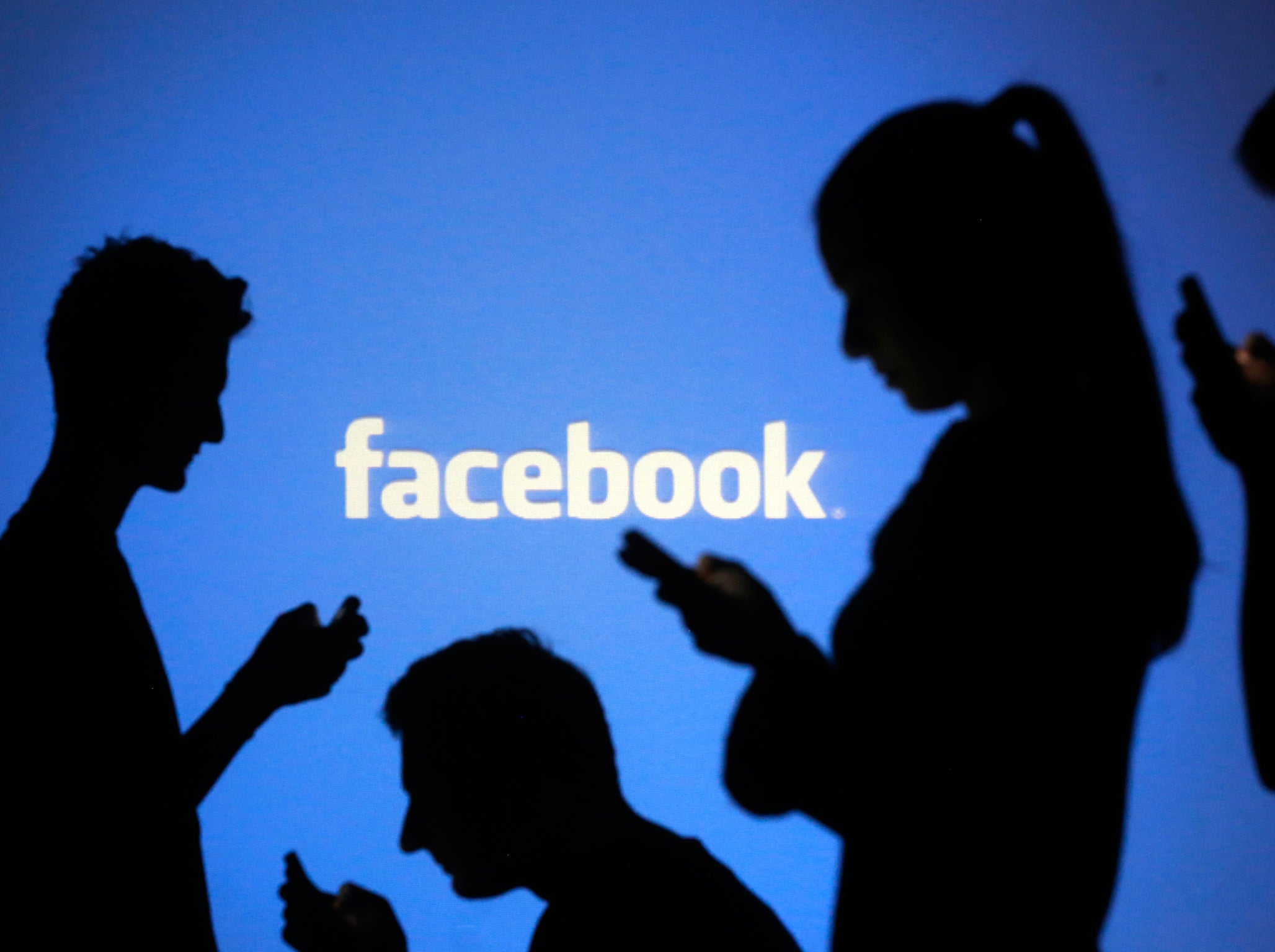 People are silhouetted as they pose with mobile devices in front of a screen projected with a Facebook logo, in this picture illustration taken in Zenica October 29, 2014