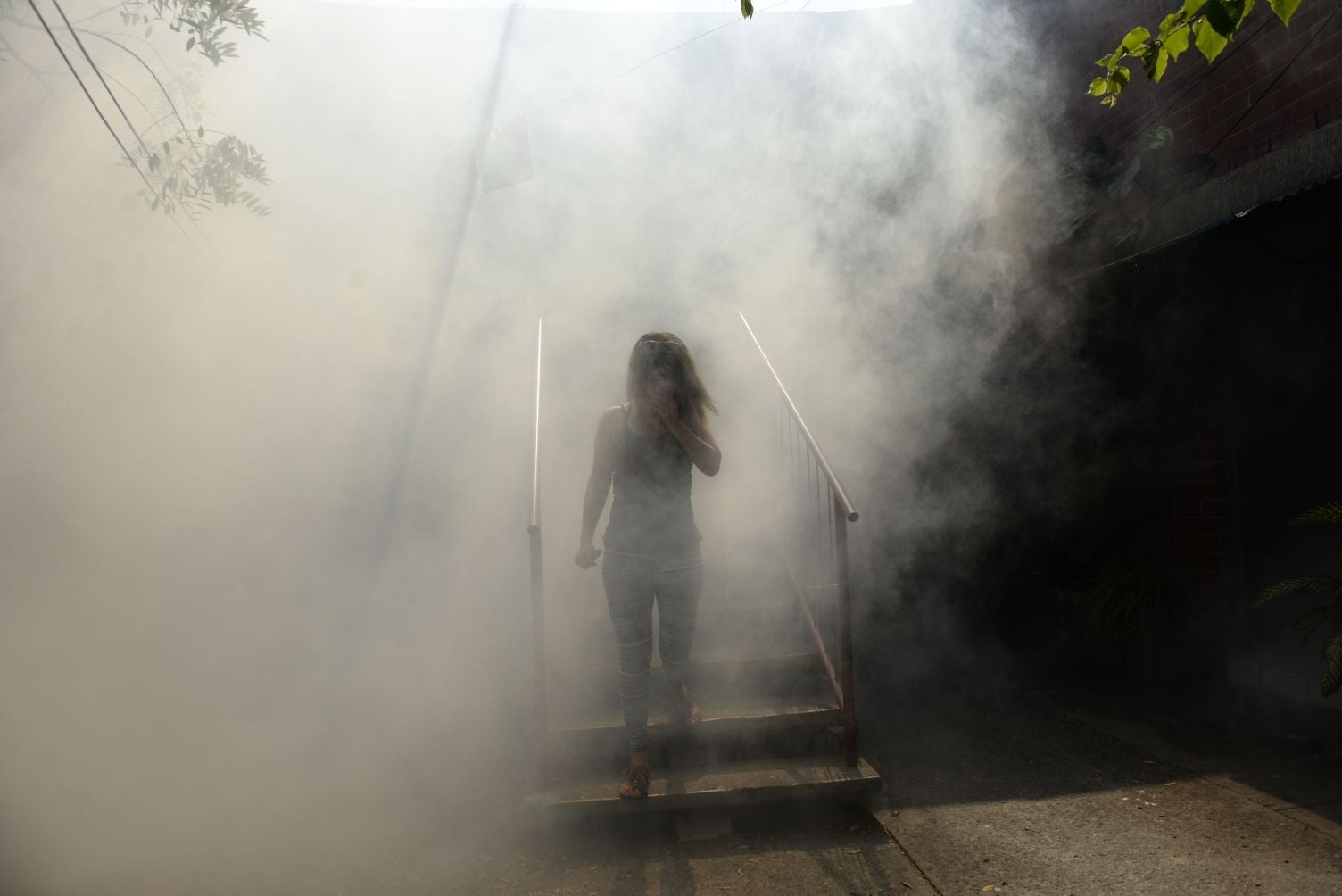 A woman walks through the fumes as Health Ministry employee fumigate against the Aedes aegypti mosquito to prevent the spread of the Zika virus in Soyapango, six km east of San Salvador