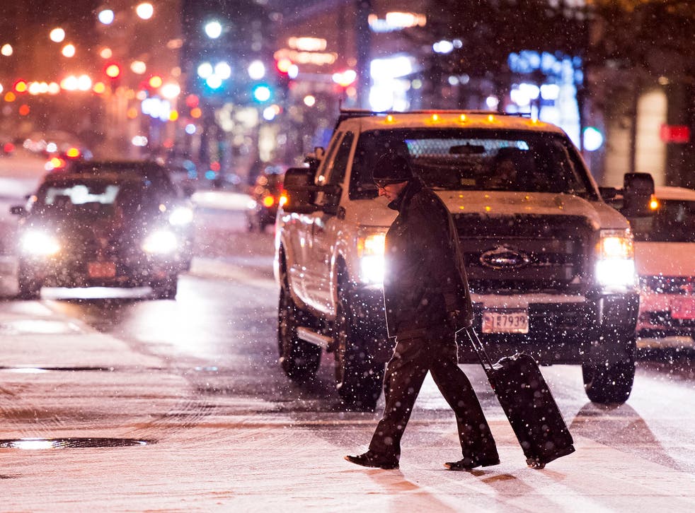 A pedestrian walks across a snow-covered road during snowfall, in downtown Washington, DC