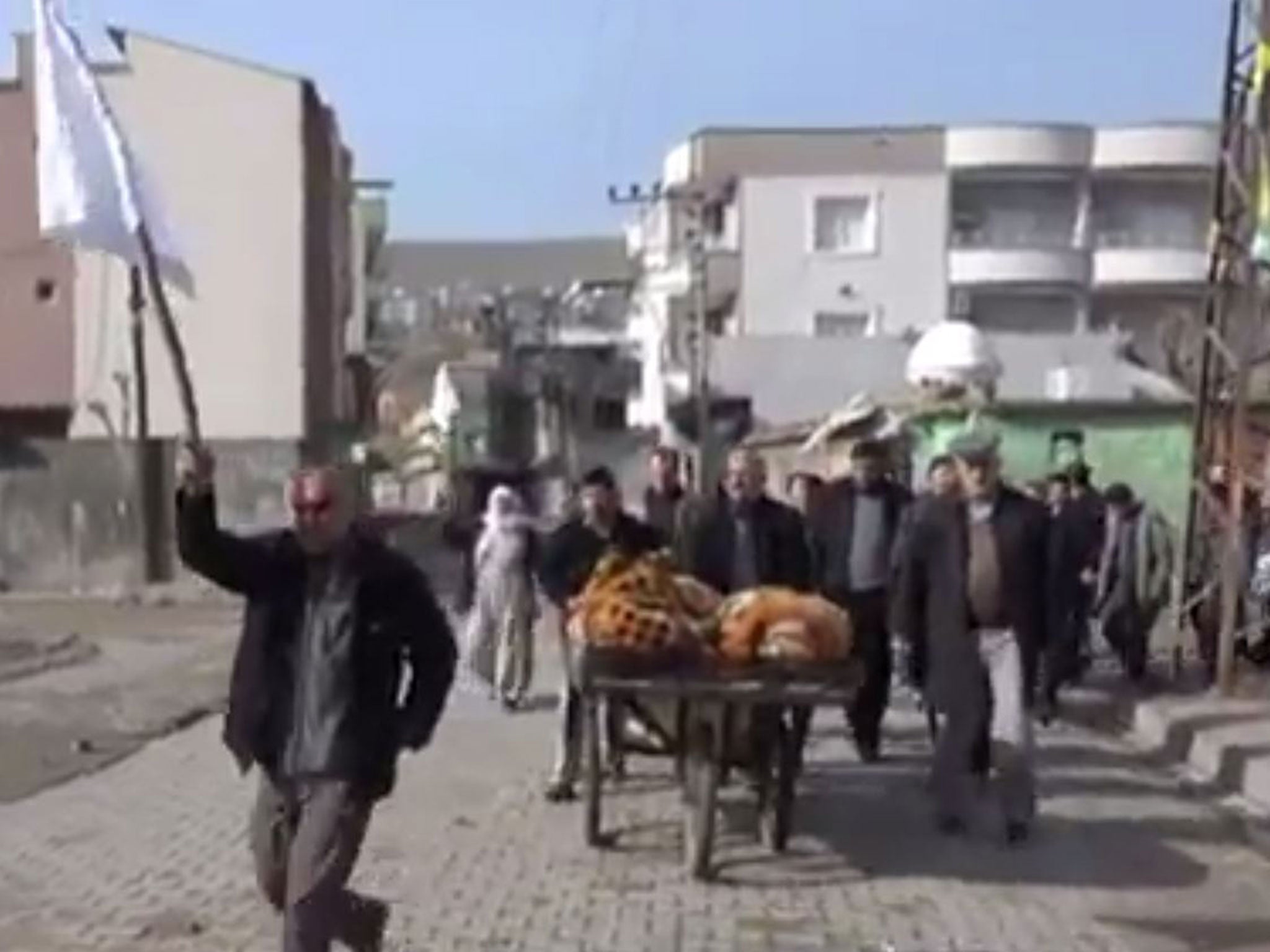 In the video, several civilians are shown waving white flags as they walk with a cart which appears to hold two covered bodies