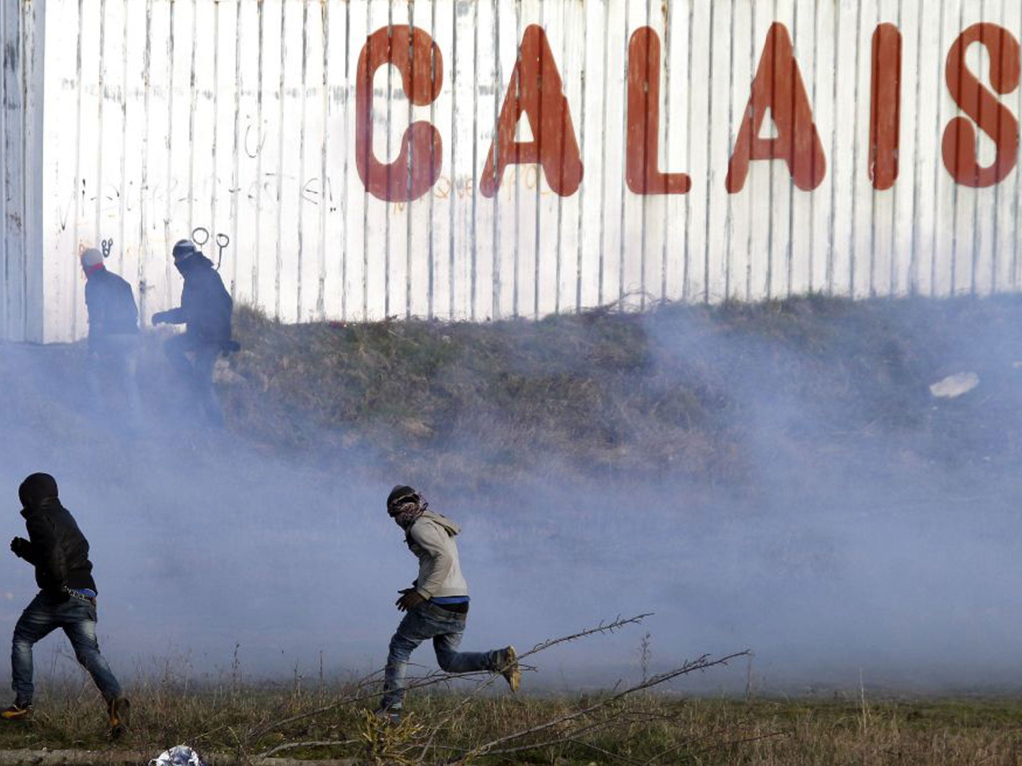 Migrants run away from tear gas thrown by police forces near the Channel Tunnel in Calais