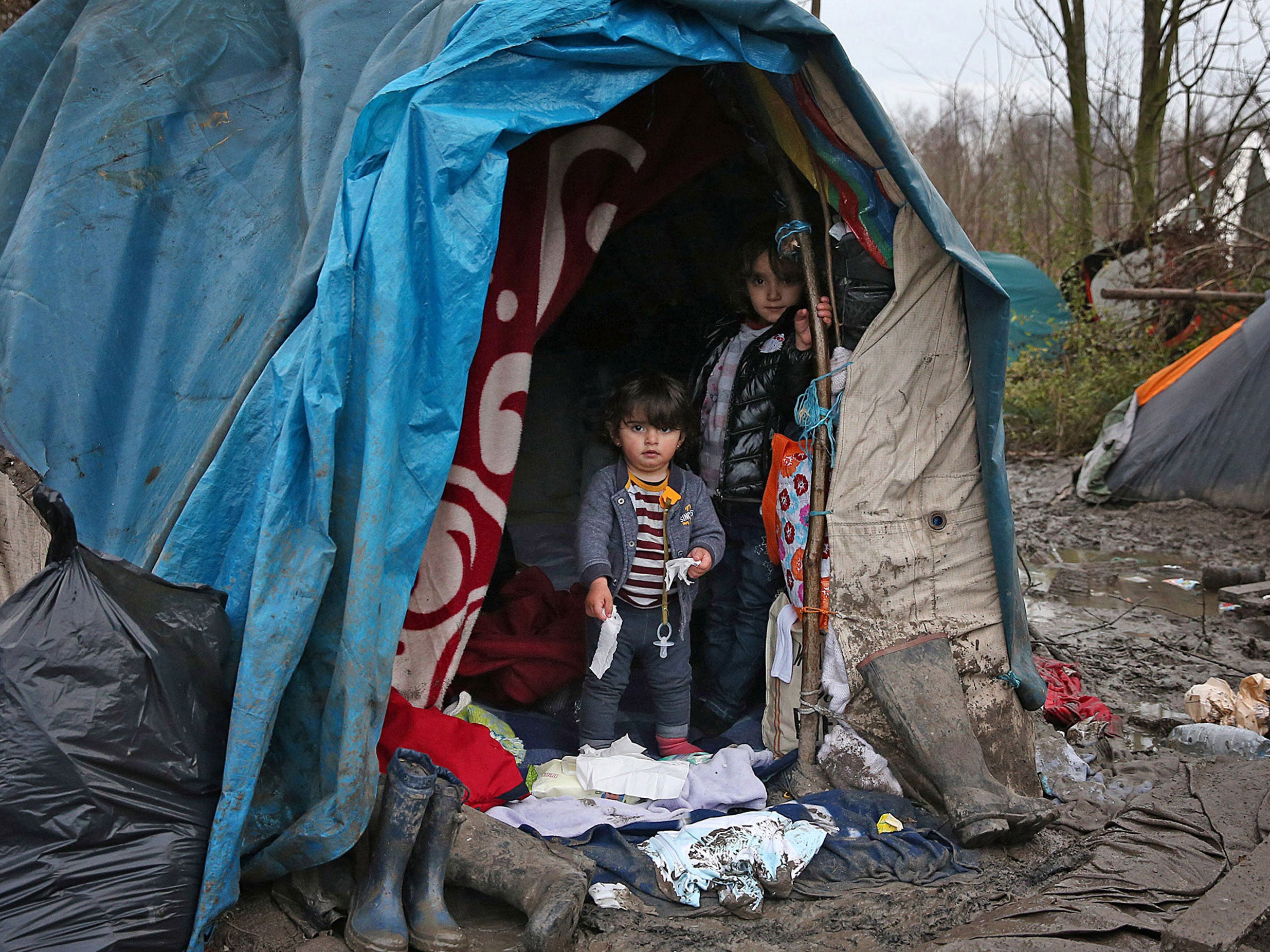 Children stand at the entrance to their shelter in a migrant camp in Dunkirk during harsh winter conditions