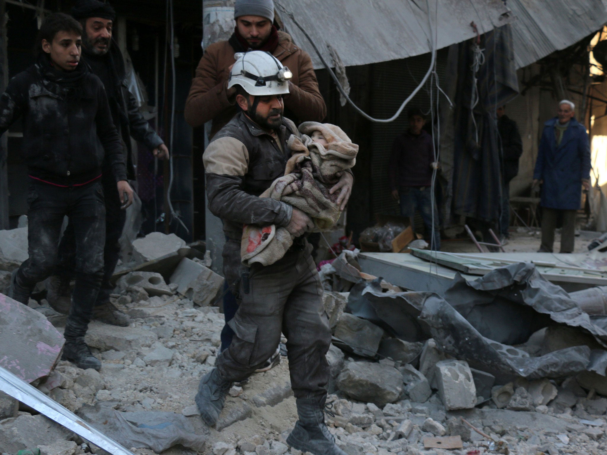 A Syrian Civil Defence worker carries a child wrapped in a blanket over the rubble following a reported air strike by Syrian government forces