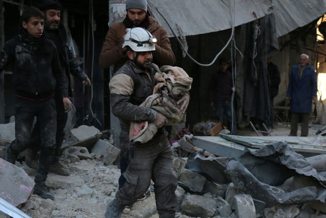 A Syrian Civil Defence worker carries a child wrapped in a blanket over the rubble following a reported air strike by Syrian government forces