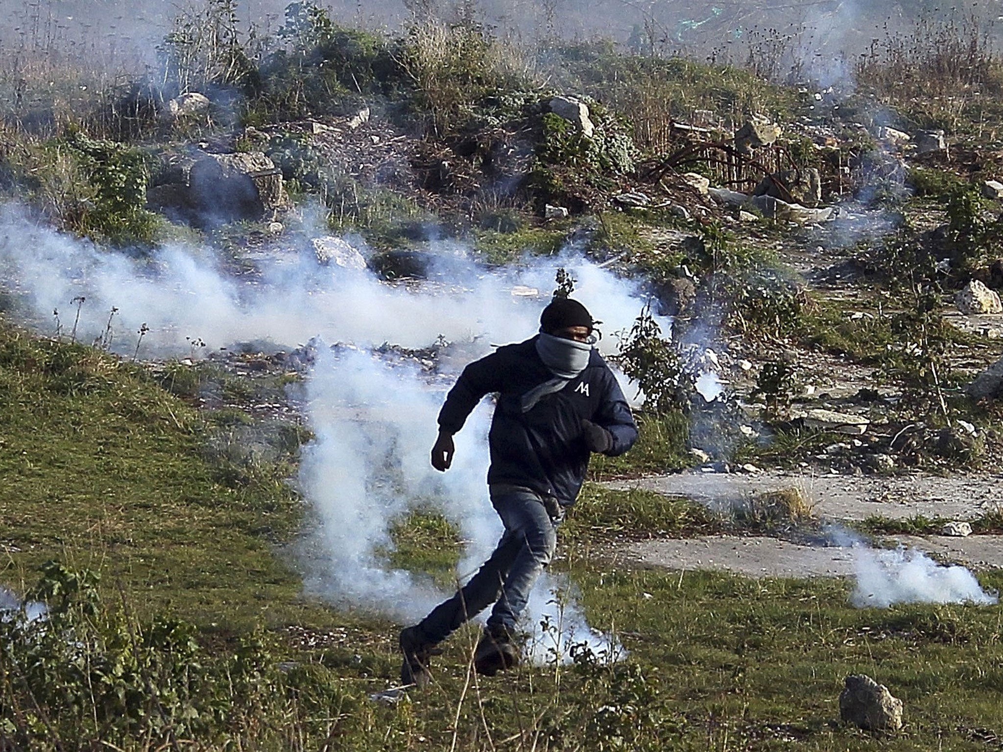 A migrant runs away from tear gas thrown by police forces near the Channel Tunnel in Calais
