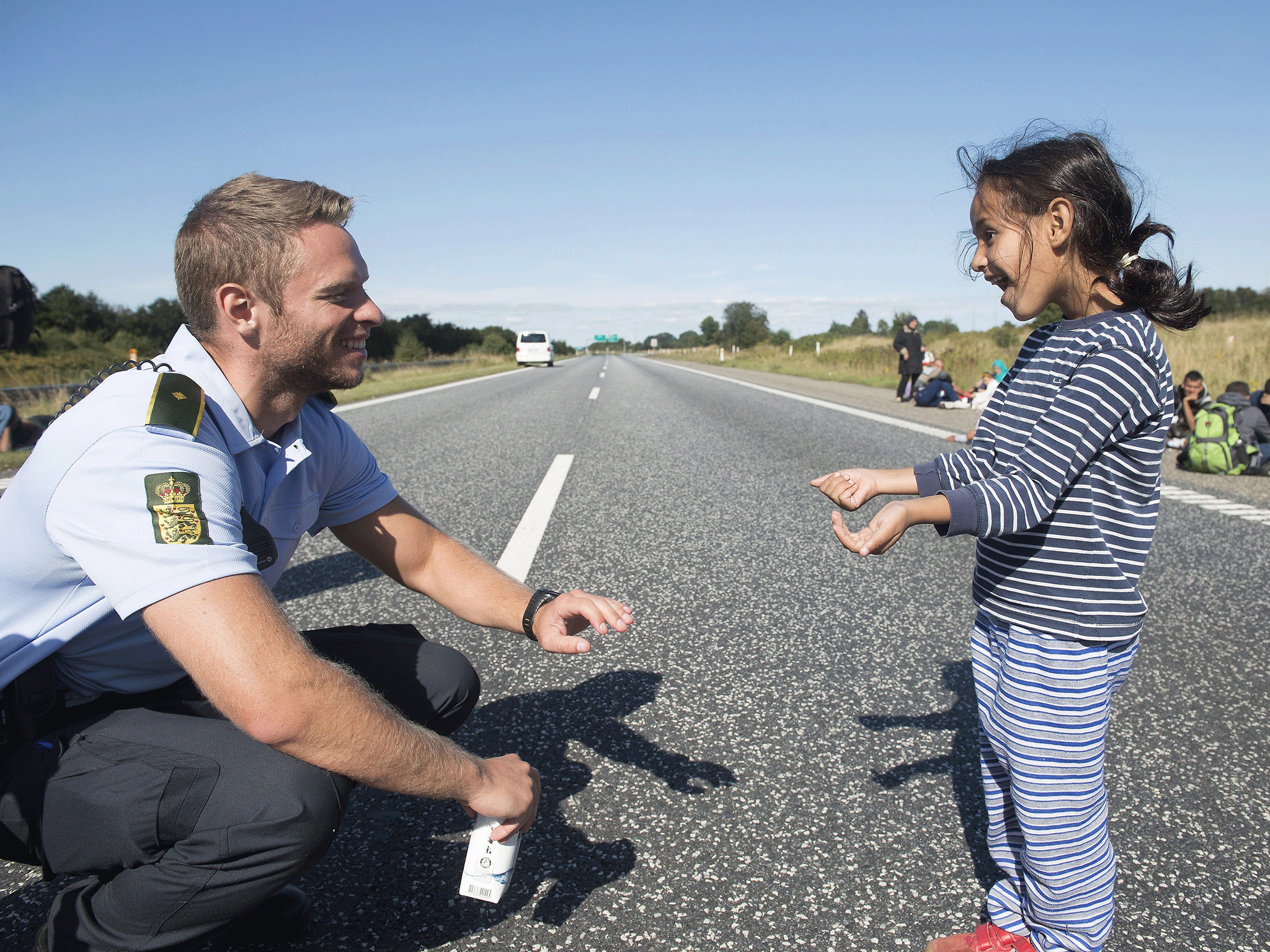 A Danish policeman plays a game with a refugee girl - who under new measures could have to wait three years to be granted asylum