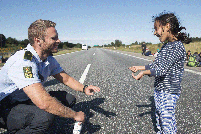 A Danish policeman plays a game with a refugee girl en route to a safer home
