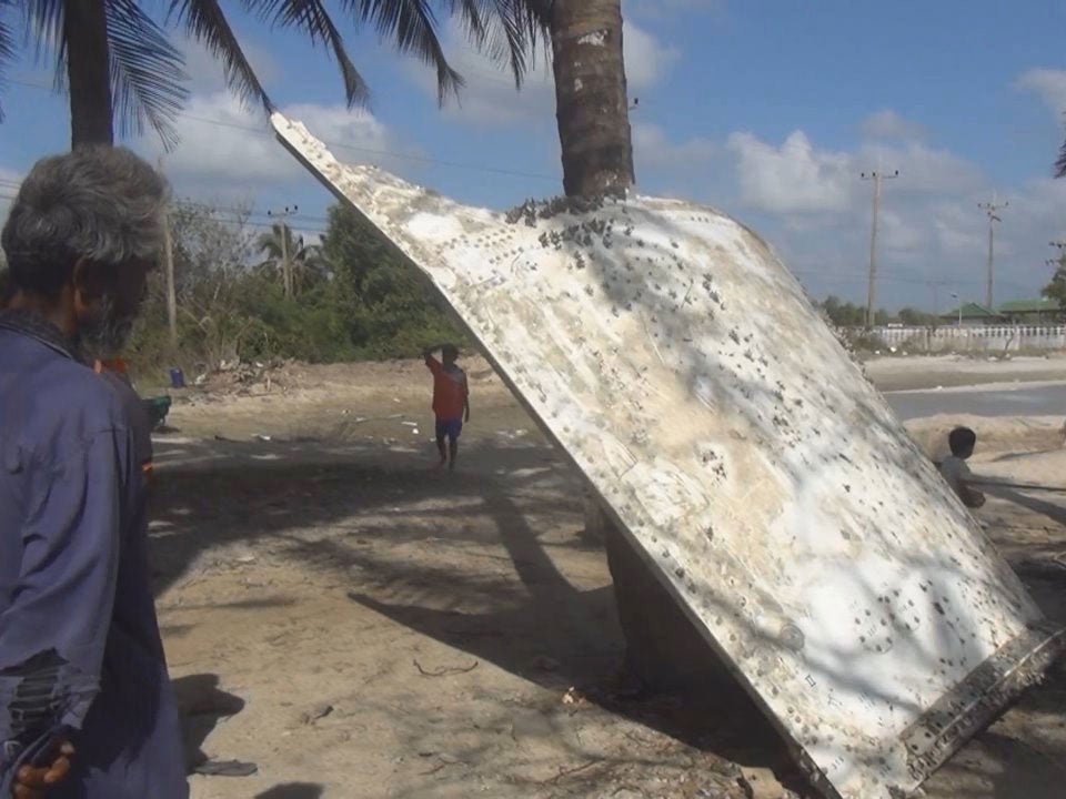 Thai people look at a large chunk of metal found on a beach in Nakhon Si Thammarat province