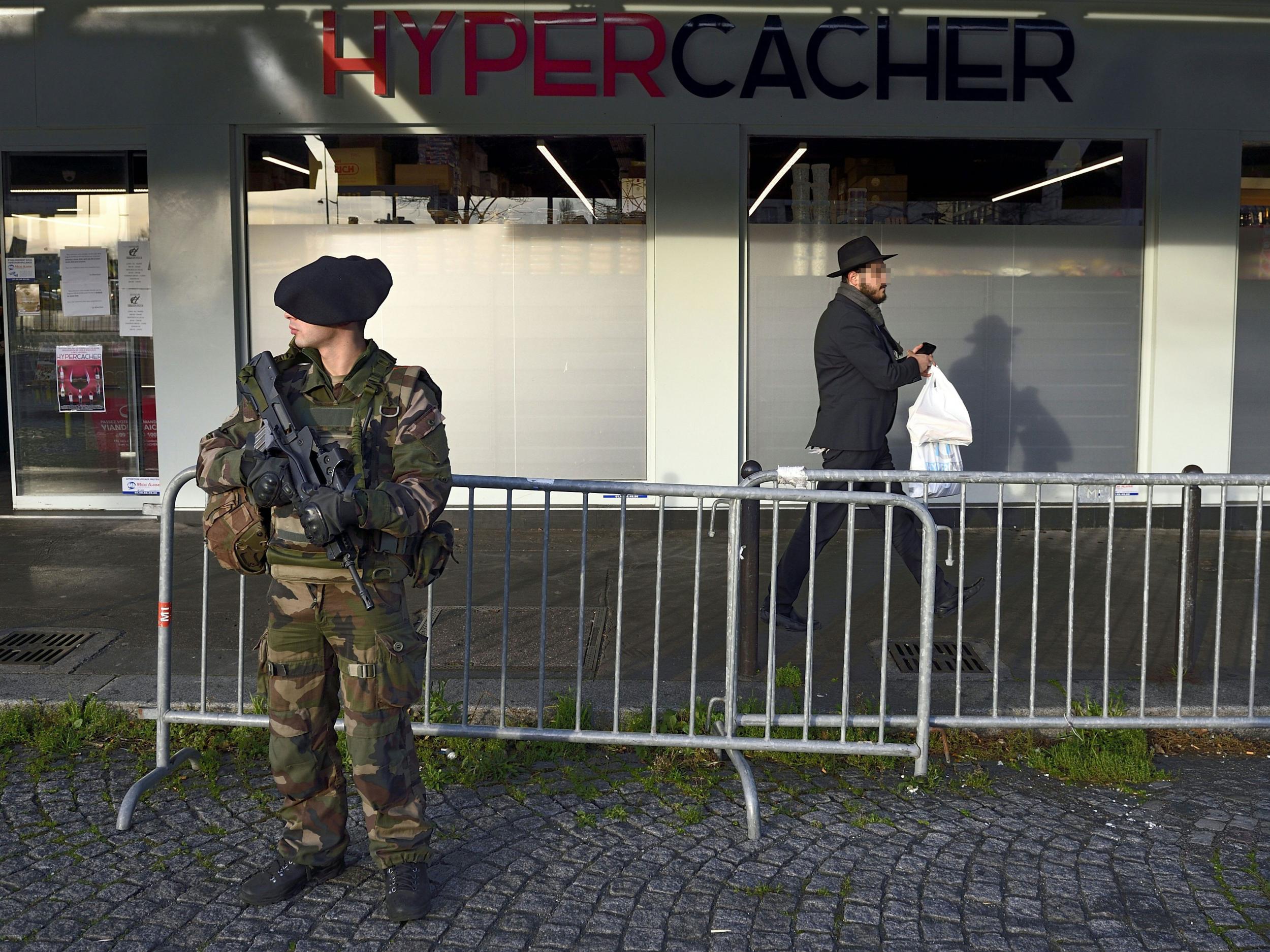 A Jewish man walks past a French soldier standing guard outside the Hypercacher kosher supermarket where four Jewish people were murdered by Islamist gunmen last January