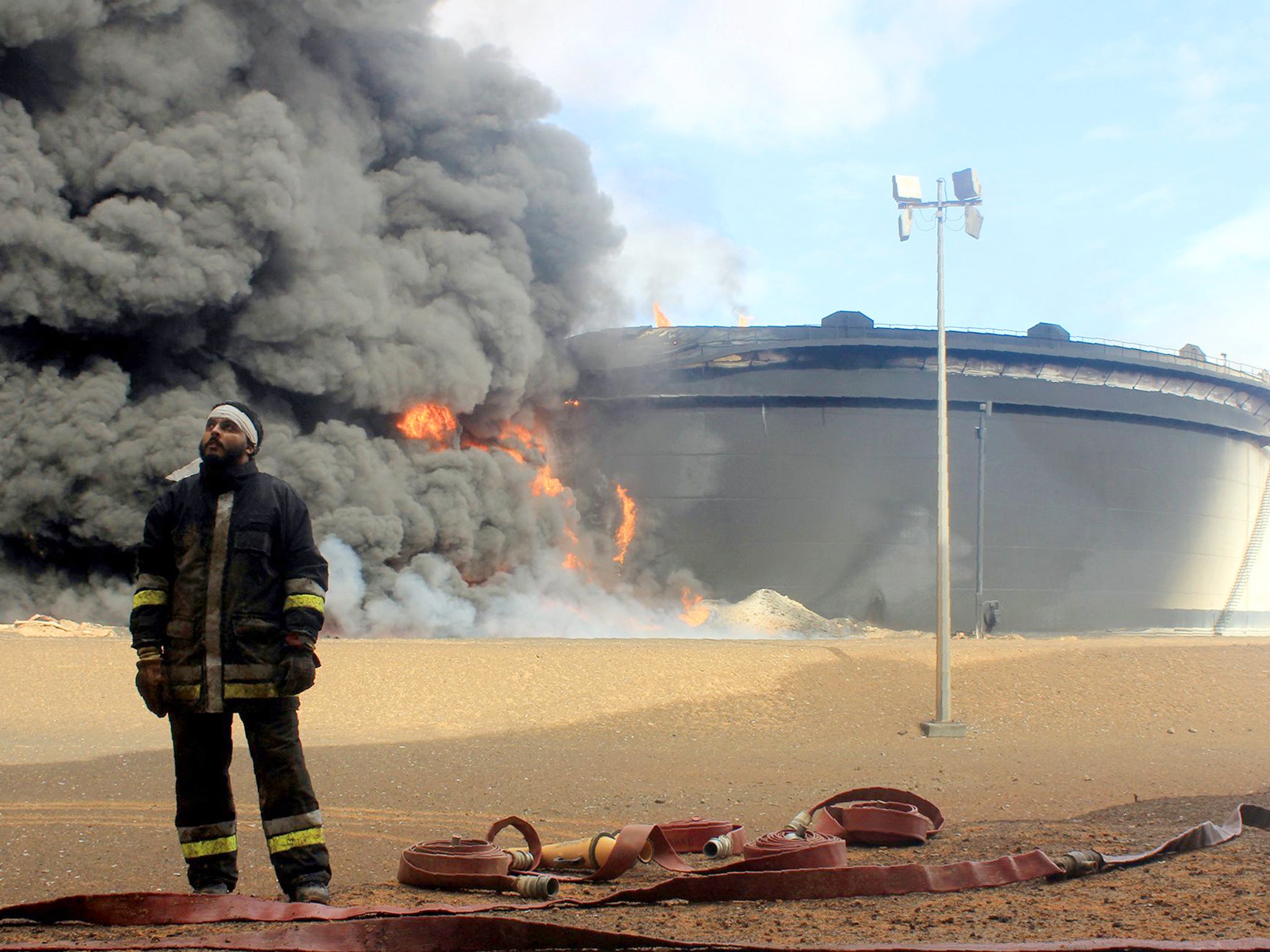 A Libyan fireman stands in front of an oil storage tank at an oil facility in northern Libya's Ras Lanouf region in February, after it was set ablaze following attacks launched by Isis jihadists (AP)