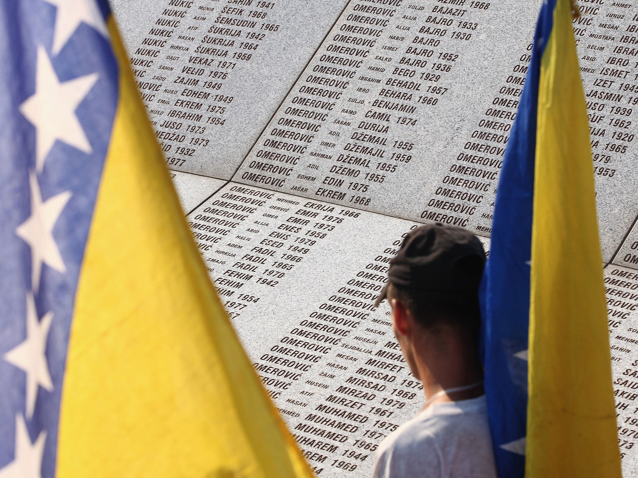 Peace marchers bearing the federal flag of Bosnia and Herzegovina walk past a stone memorial bearing the names of victims of the 1995 Srebrenica massacre at the Potocari cemetery and memorial near Srebrenica on 10 July, 2011