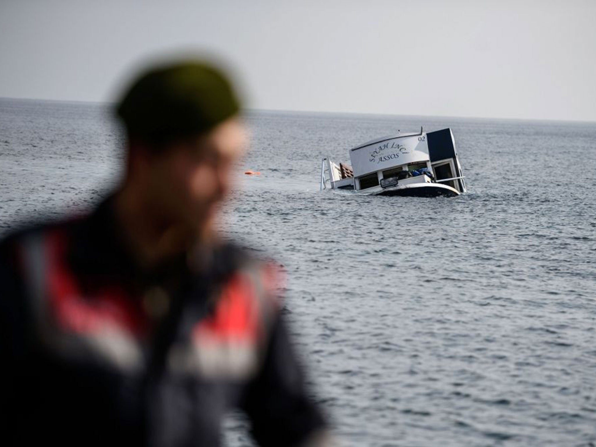 The sinking boat is seen behind a Turkish gendarme off the coast of Canakkale's Bademli district on January 30, 2016.