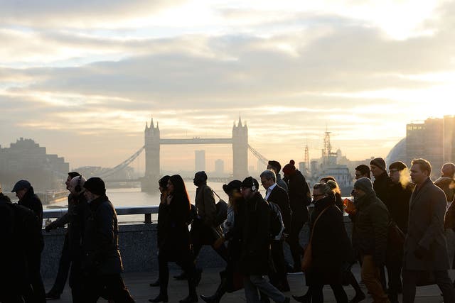 Commuters walk on London Bridge at sunrise with Tower Bridge in the background