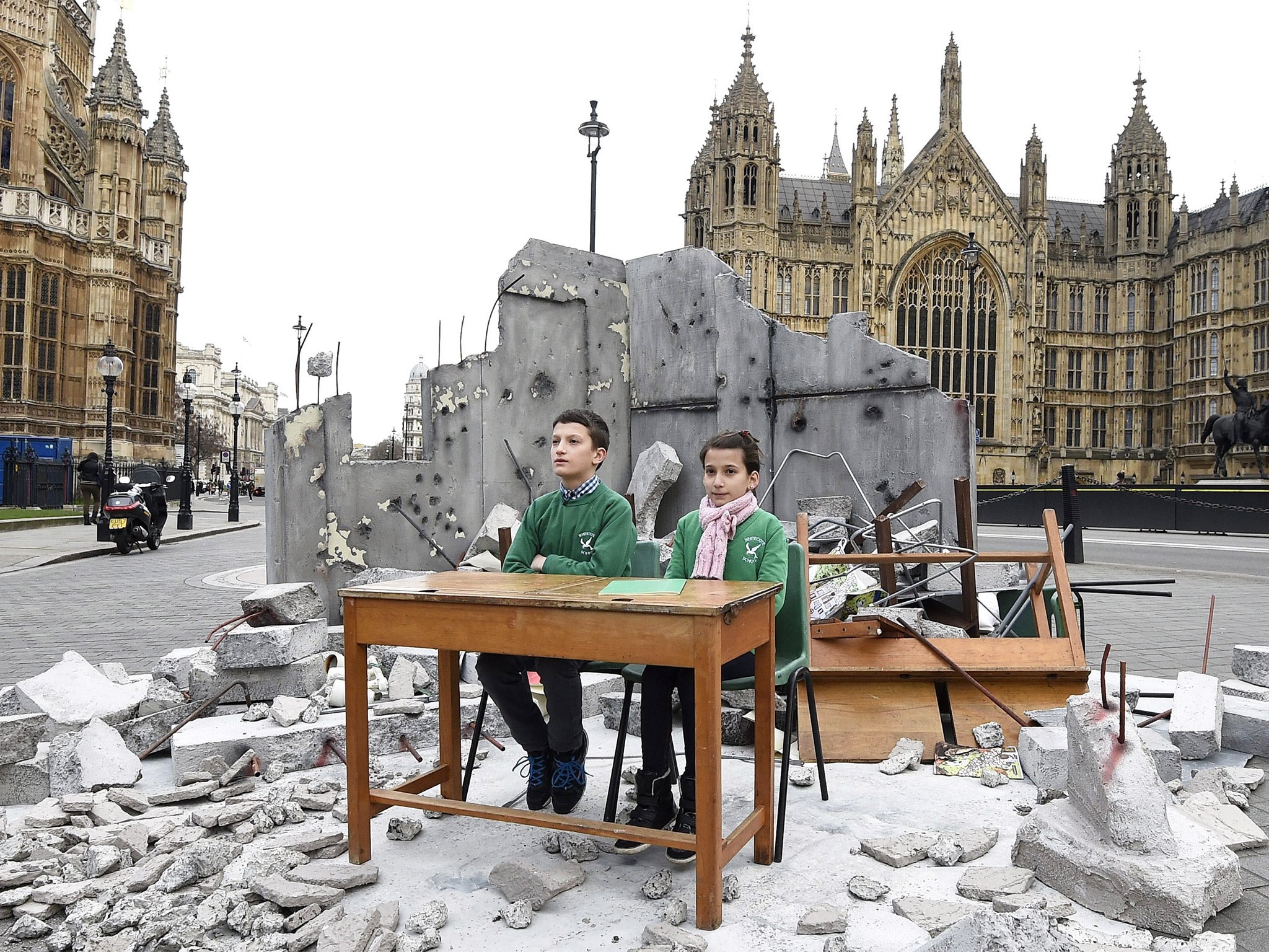 Abdallah, 12, and Dania, 10, whose school was bombed in Aleppo, sit in a mock up of a destroyed classroom, outside the Houses of Parliament in London
