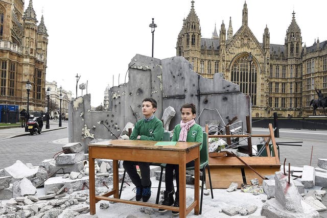 Abdallah, 12, and Dania, 10, whose school was bombed in Aleppo, sit in a mock up of a destroyed classroom, outside the Houses of Parliament in London