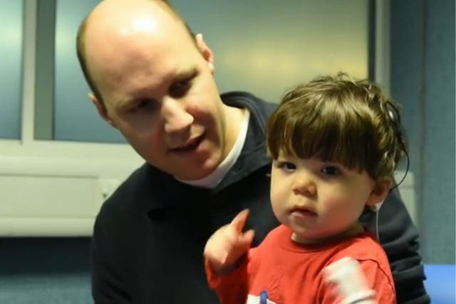 Alfie sits on his fathers knee while his new cochlear implant fitted and switched on for the first time