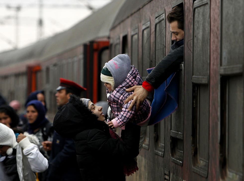 A refugee man passes a baby to a woman from a train window, upon their arrival at the transit center for refugees near northern Macedonian village of Tabanovce