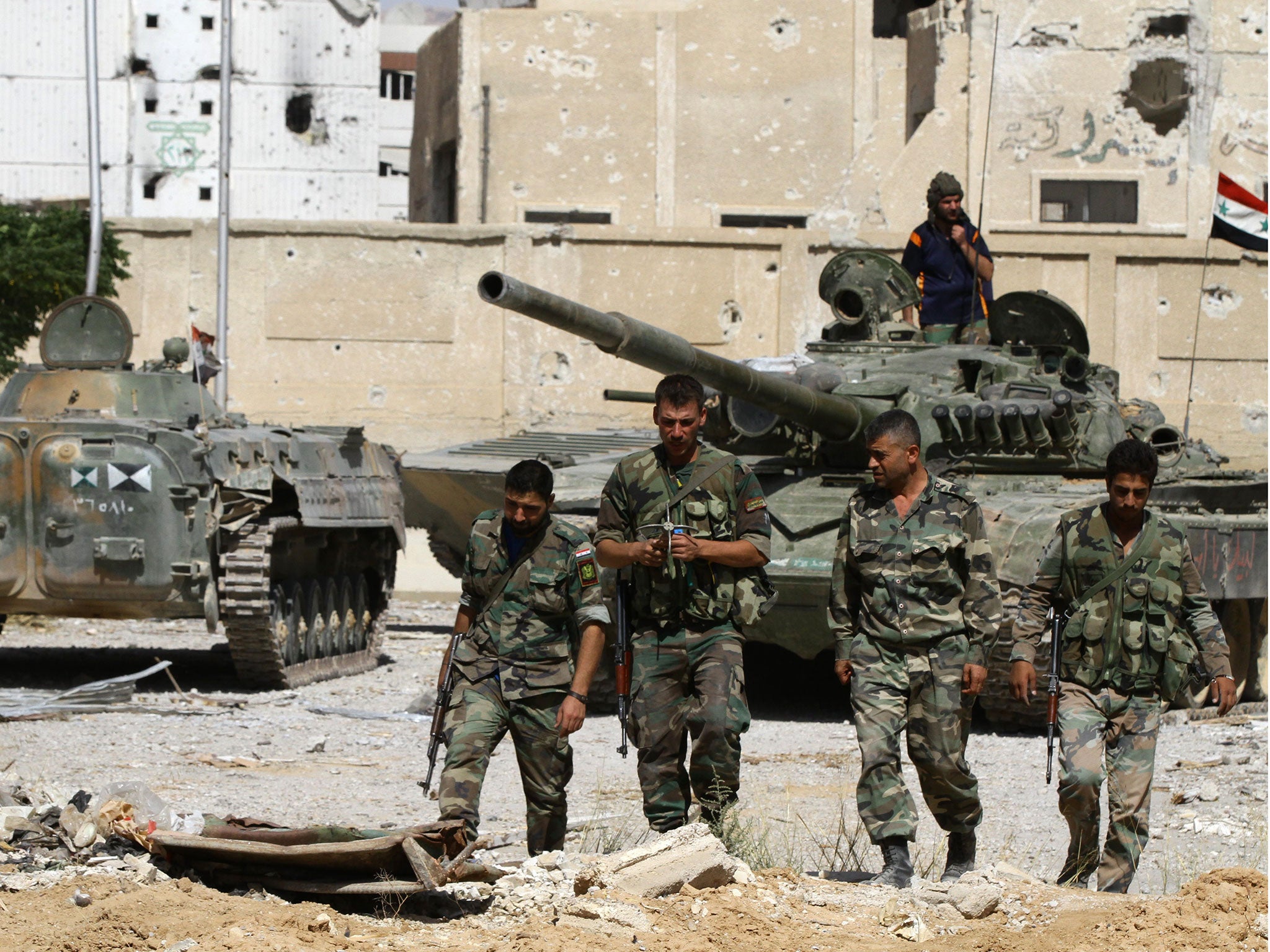 Syrian government soldiers walk near tanks parked in front of damaged buildings in Adra northeast of the capital Damascus on 25 September, 2014