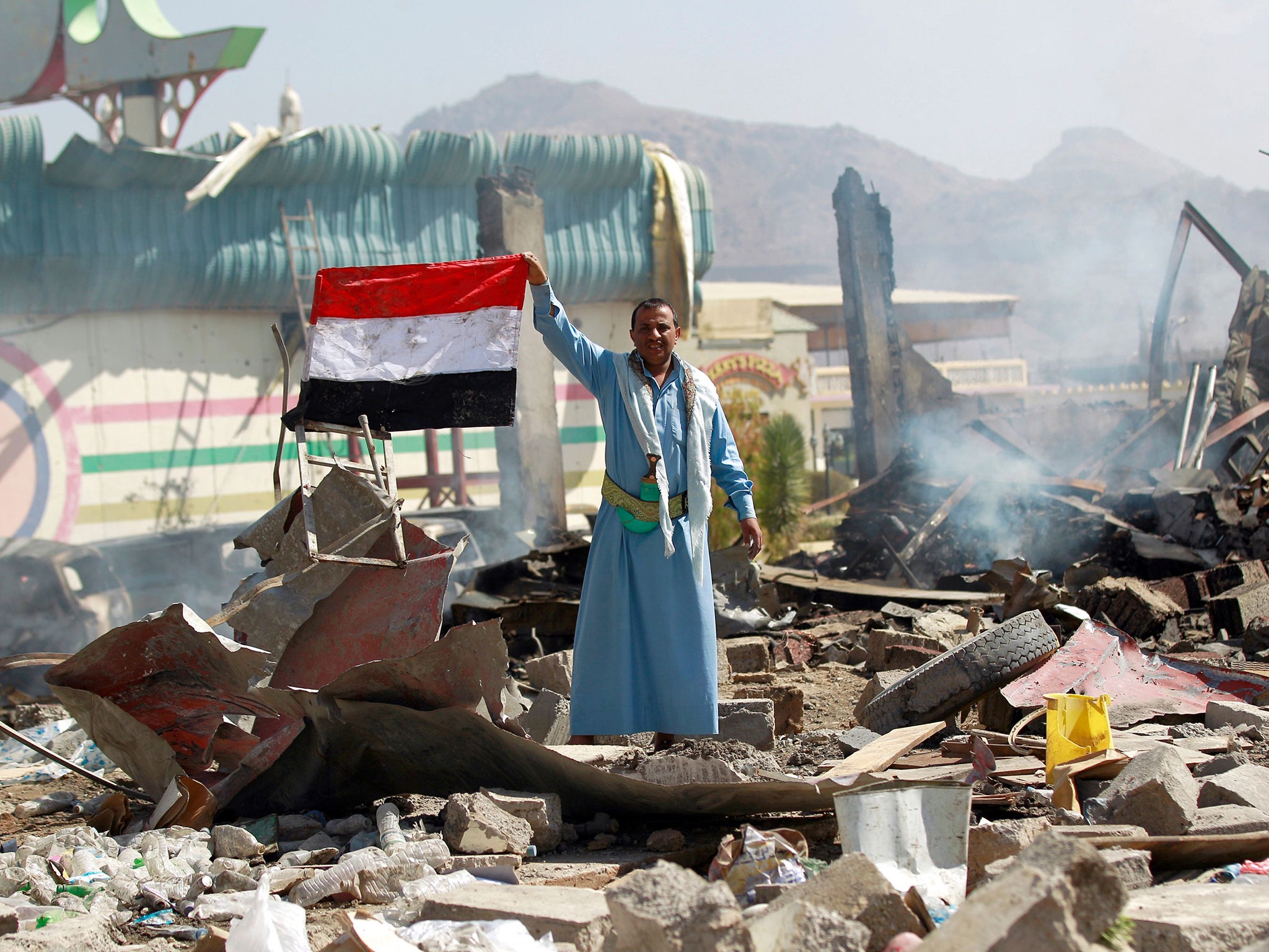 A Yemeni man waves his national flag as he stands amid the ruins of a school and a bowling club hit by an air-strike carried out by the Saudi-led coalition, in the capital Sanaa,
