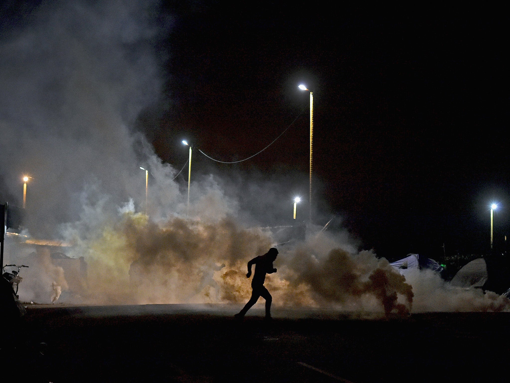 A refugee flees police tear gas near the entrance to the Jungle camp in Calais